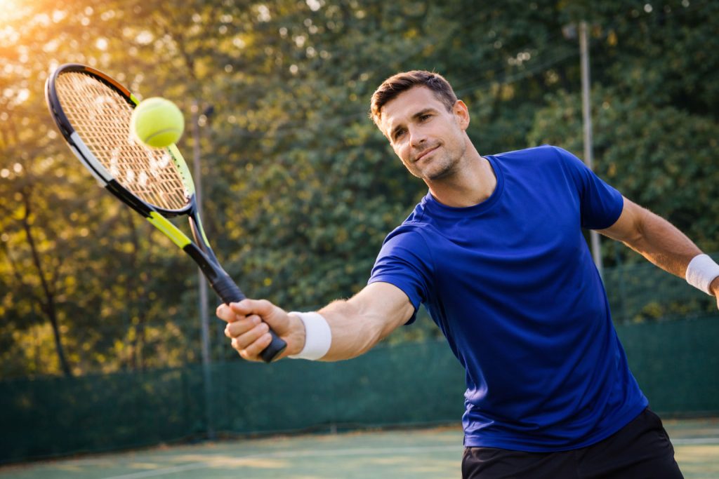Profesor de tenis peloteando en una pista exterior durante una sesión de entrenamiento
